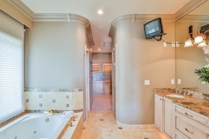 Un baño moderno con una bañera grande, un tocador con lavabo y un televisor montado en la pared.