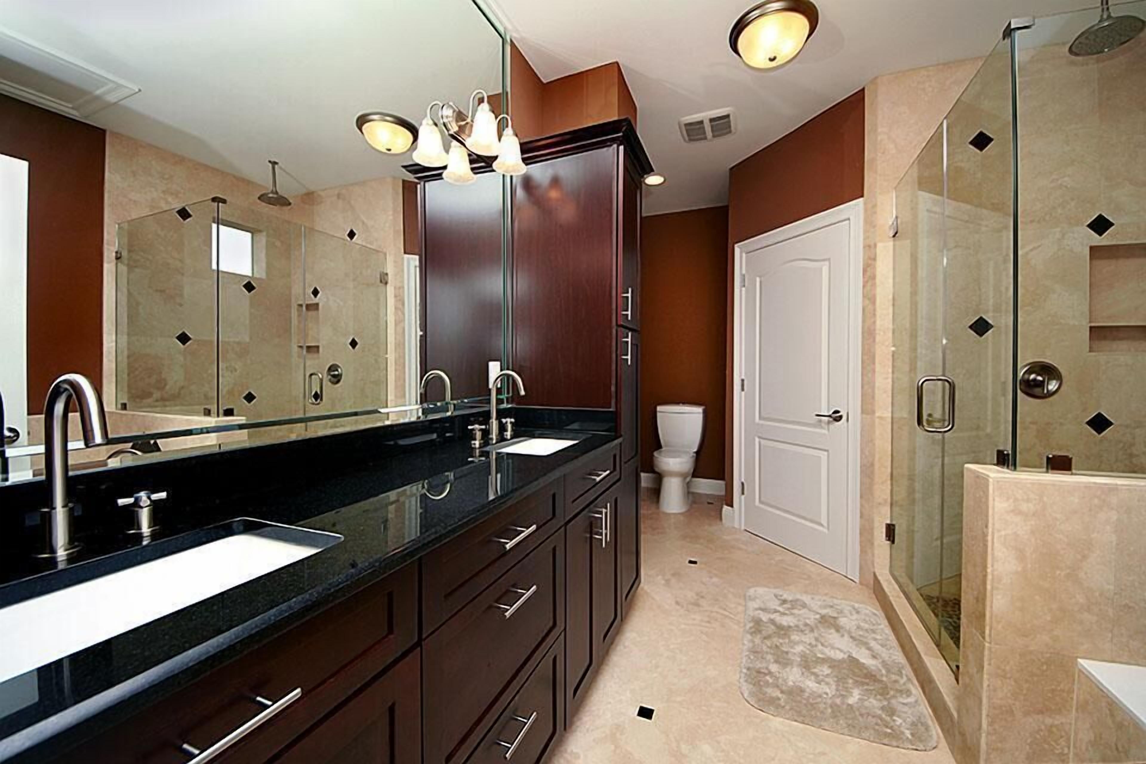 A modern bathroom with a double sink vanity, a glass shower enclosure, and a toilet.