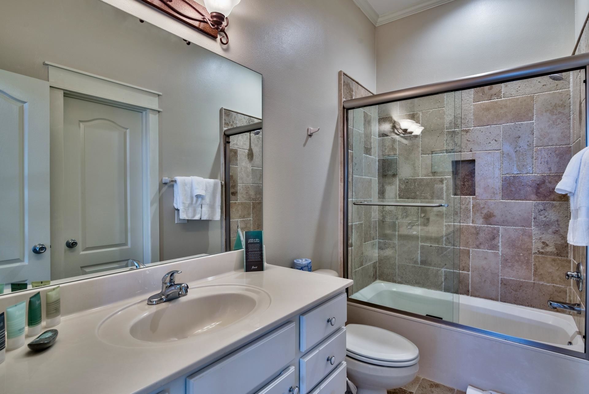 A modern bathroom with a large mirror, a sink, a toilet, and a glass-enclosed shower.