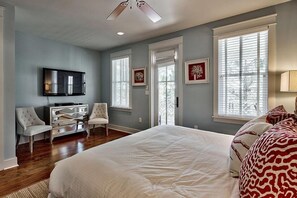 A bedroom with a large bed, a television mounted on the wall, and two chairs.