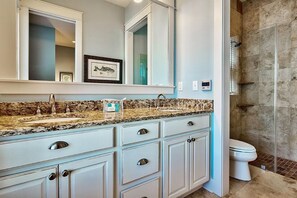 A bathroom with a granite countertop, white cabinets, a large mirror, and a glass shower enclosure.
