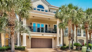 A two-story house with a garage, surrounded by palm trees and a clear sky.
