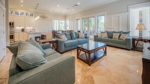 A spacious living area with two sofas and a coffee table, a dining area with chairs, and a kitchen with white cabinets.