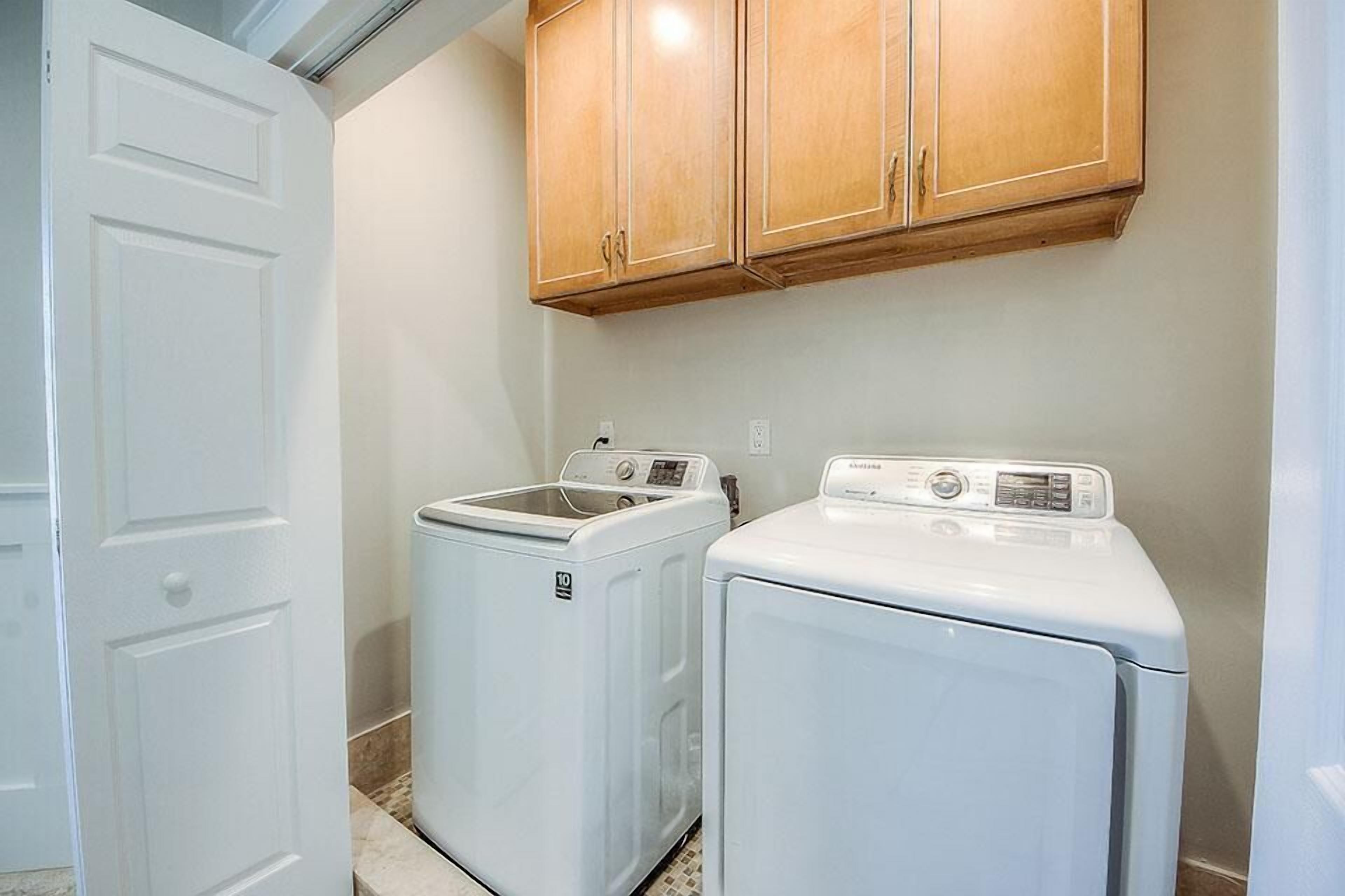A laundry room with two front-loading washing machines, wooden cabinets above, and a white door.