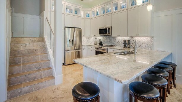 A modern kitchen with white cabinetry, a stainless steel refrigerator, a microwave, and a large island with bar stools.