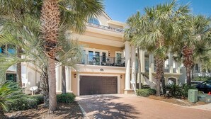 A multi-story residential building with a large garage, palm trees, and a clear sky.