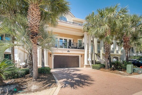 A multi-story residential building with a large garage, palm trees, and a clear sky.