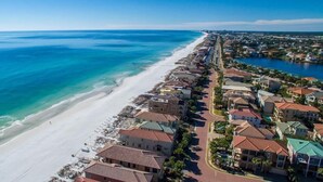 An aerial view of a coastal residential area with a beachfront, houses with red roofs, and a clear blue sky.