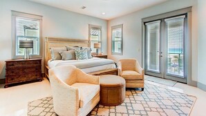 A bedroom with a large bed, two chairs, a wooden nightstand, and a patterned rug. - DaShells30A 6 Bedroom Holiday Home by Five Star Properties (Santa Rosa Beach)