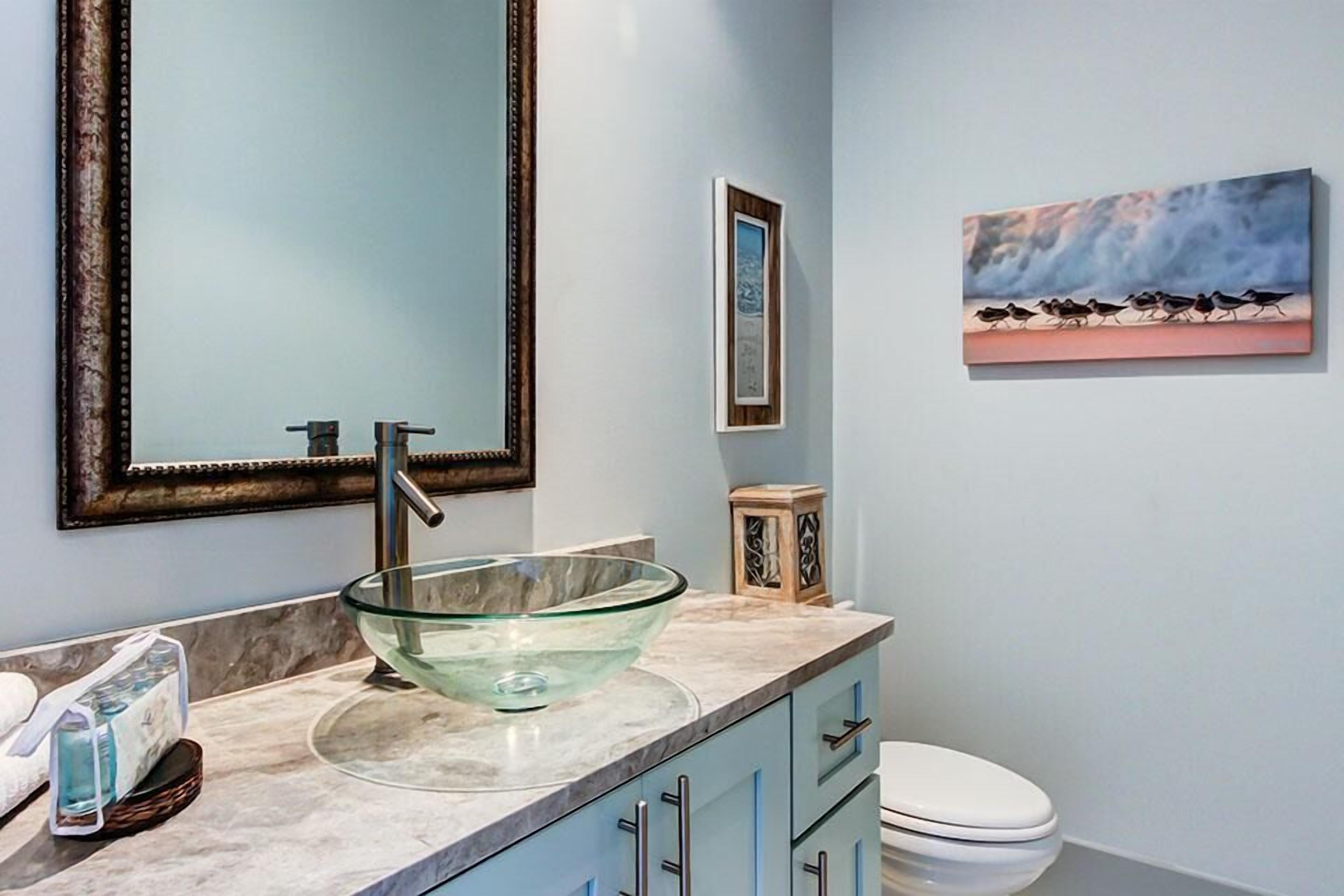 Une salle de bain avec un lavabo en forme de bol en verre, un grand miroir, un tableau encadré au mur et des toilettes.