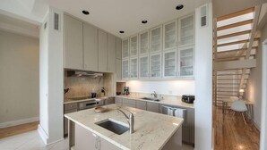 A modern kitchen with a central island, built-in cabinets, and a wooden staircase. - Desire 4 Bedroom Holiday Home by Five Star Properties (Santa Rosa Beach)