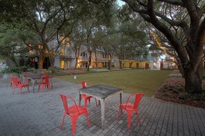 An outdoor patio area with a wooden table and red chairs, surrounded by trees and a well-maintained lawn. - Desire 4 Bedroom Holiday Home by Five Star Properties (Santa Rosa Beach)