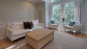 A spacious living room with a white sofa, two armchairs, a wicker ottoman, and large windows with curtains. - Desire 4 Bedroom Holiday Home by Five Star Properties (Santa Rosa Beach)