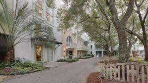 A brick pathway leading to a row of white buildings with balconies, surrounded by trees and plants. - Desire 4 Bedroom Holiday Home by Five Star Properties (Santa Rosa Beach)