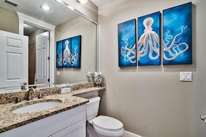 Ein Badezimmer mit Waschbecken auf Marmorplatte, Toilette in Weiß und drei blauen Bildern von Oktopussen an der Wand.