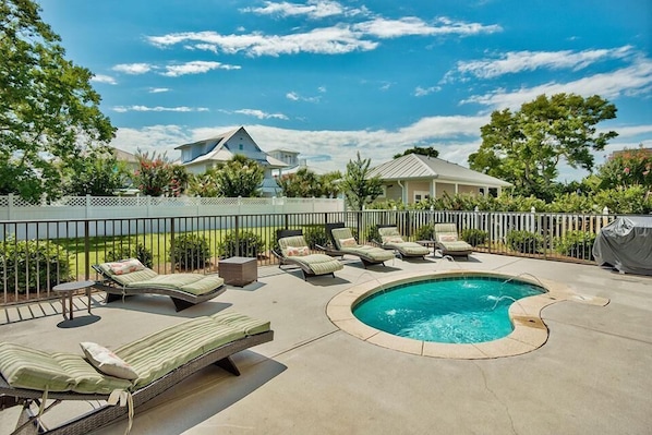 A backyard with a swimming pool, lounge chairs, and a fenced area.