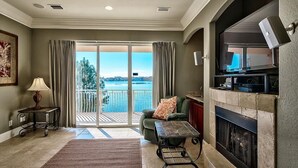 A living room with a fireplace, a sofa, a coffee table, and a view of a body of water through large sliding glass doors. - Destiny Tranquility 5 Bedroom Holiday Home by Five Star Properties (Destin)