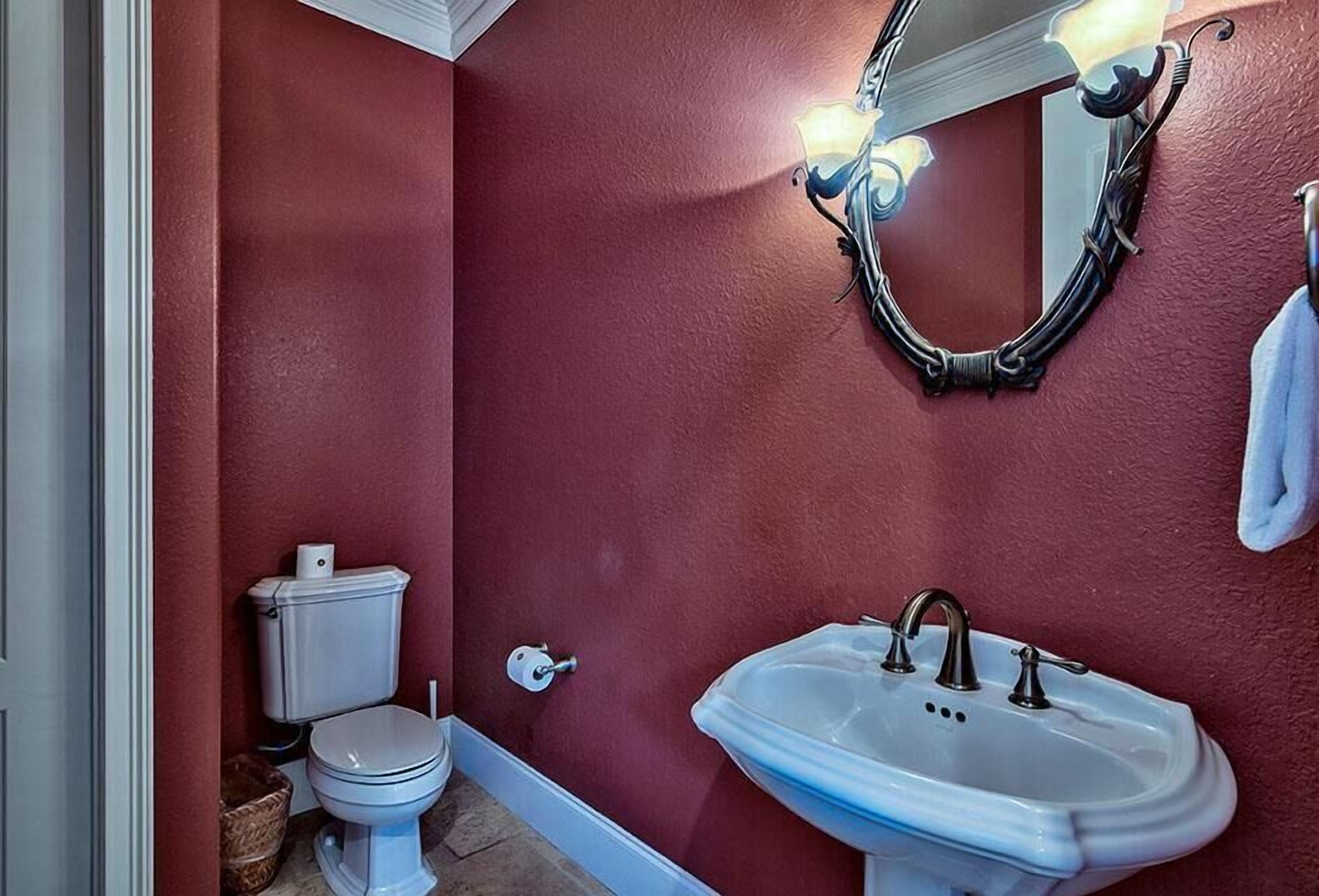 Un baño con pared roja, inodoro blanco y lavabo blanco con espejo encima.