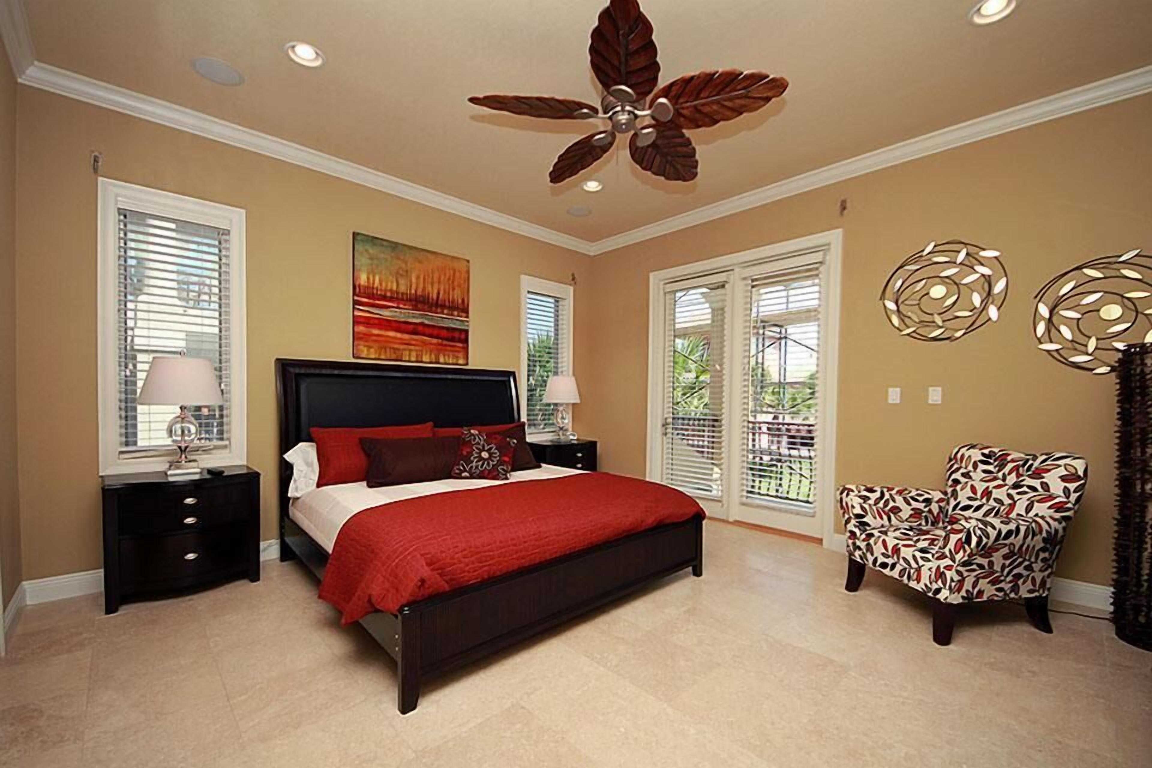 A bedroom with a bed, nightstands, a chair, a ceiling fan, and artwork on the walls.