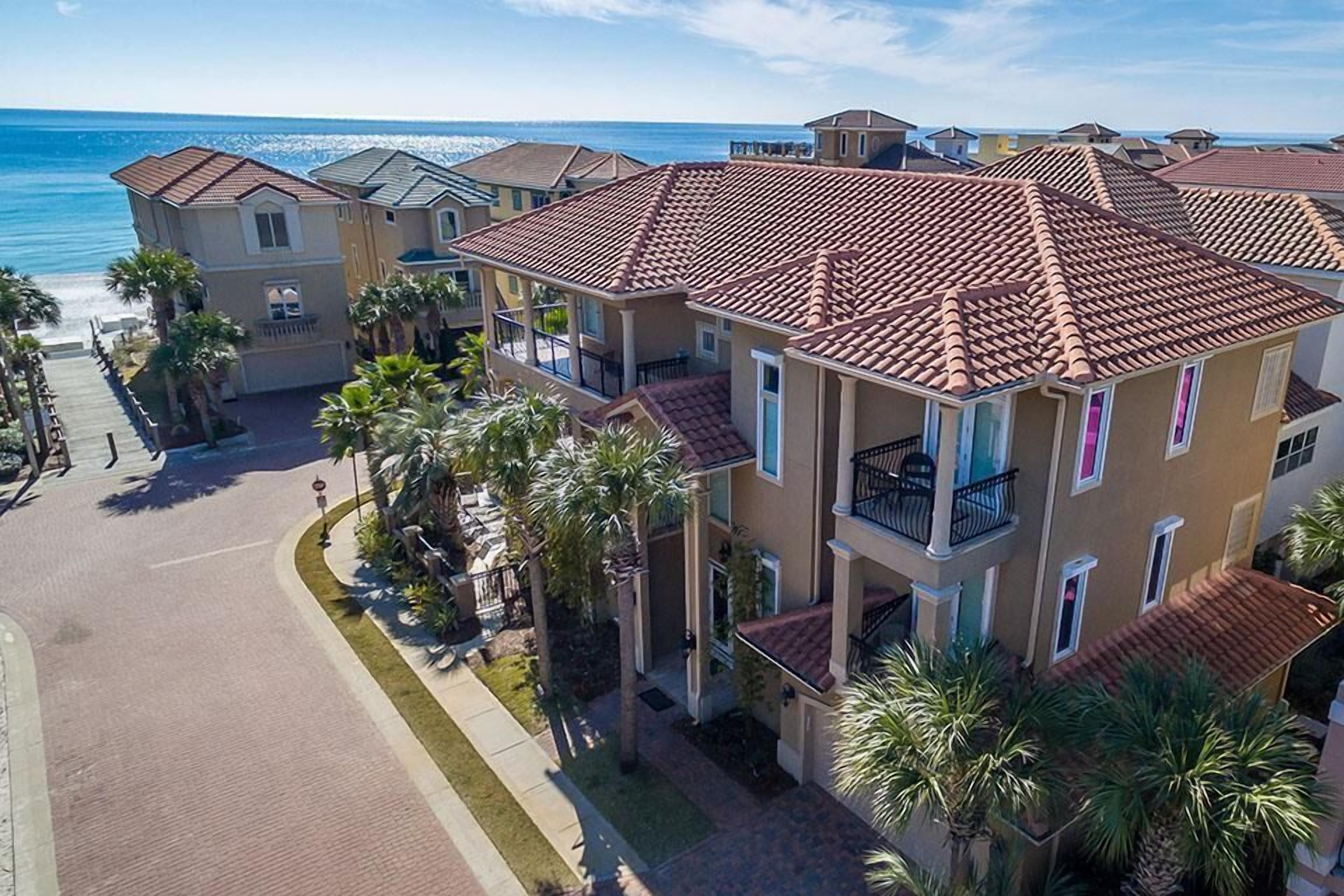 A multi-story residential building with a red-tiled roof, balconies, and a view of the beach.