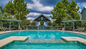 Une piscine avec un kiosque au centre, entourée d’arbres et de chaises longues.