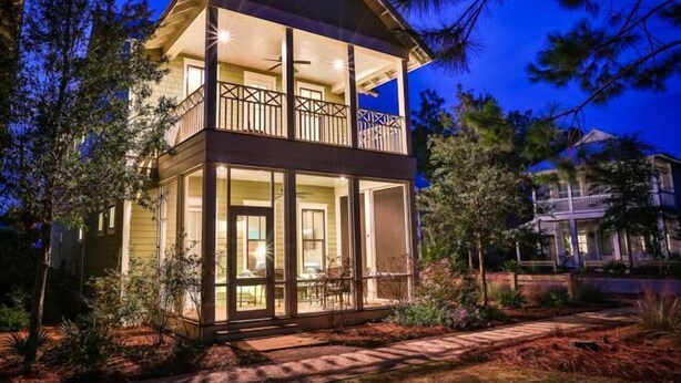 Une maison à deux étages dotée d’un balcon, entourée d’arbres et d’un jardin bien entretenu.