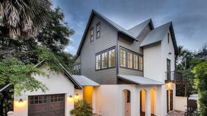 A modern two-story house with a garage, a covered patio, and a small outdoor seating area. - Dream Weaver 5 Bedroom Holiday Home by Five Star Properties (Santa Rosa Beach)