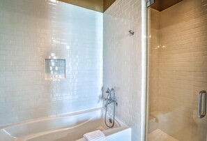 Un baño moderno con azulejos blancos tipo metro, ducha con mampara de vidrio y bañera blanca.