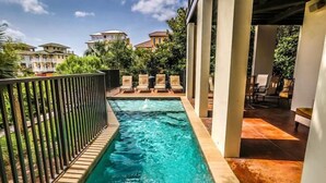 A swimming pool with a black metal fence, surrounded by lounge chairs and a view of buildings in the background. - Dream Weaver 5 Bedroom Holiday Home by Five Star Properties (Santa Rosa Beach)