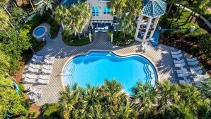 A resort with a large swimming pool, lounge chairs, palm trees, and a building with a blue roof. - Emerald Enchantment 4 Bedroom Holiday Home by Five Star Properties (Destin)