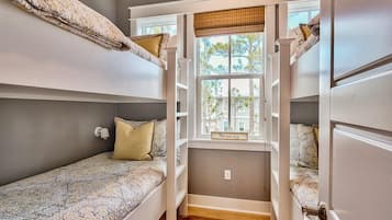 A dorm-style room with bunk beds, a window with a view of trees, and a small shelf with a sign.