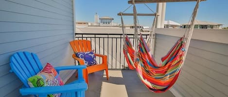 A balcony with two blue Adirondack chairs, one orange chair, and a colorful hammock.