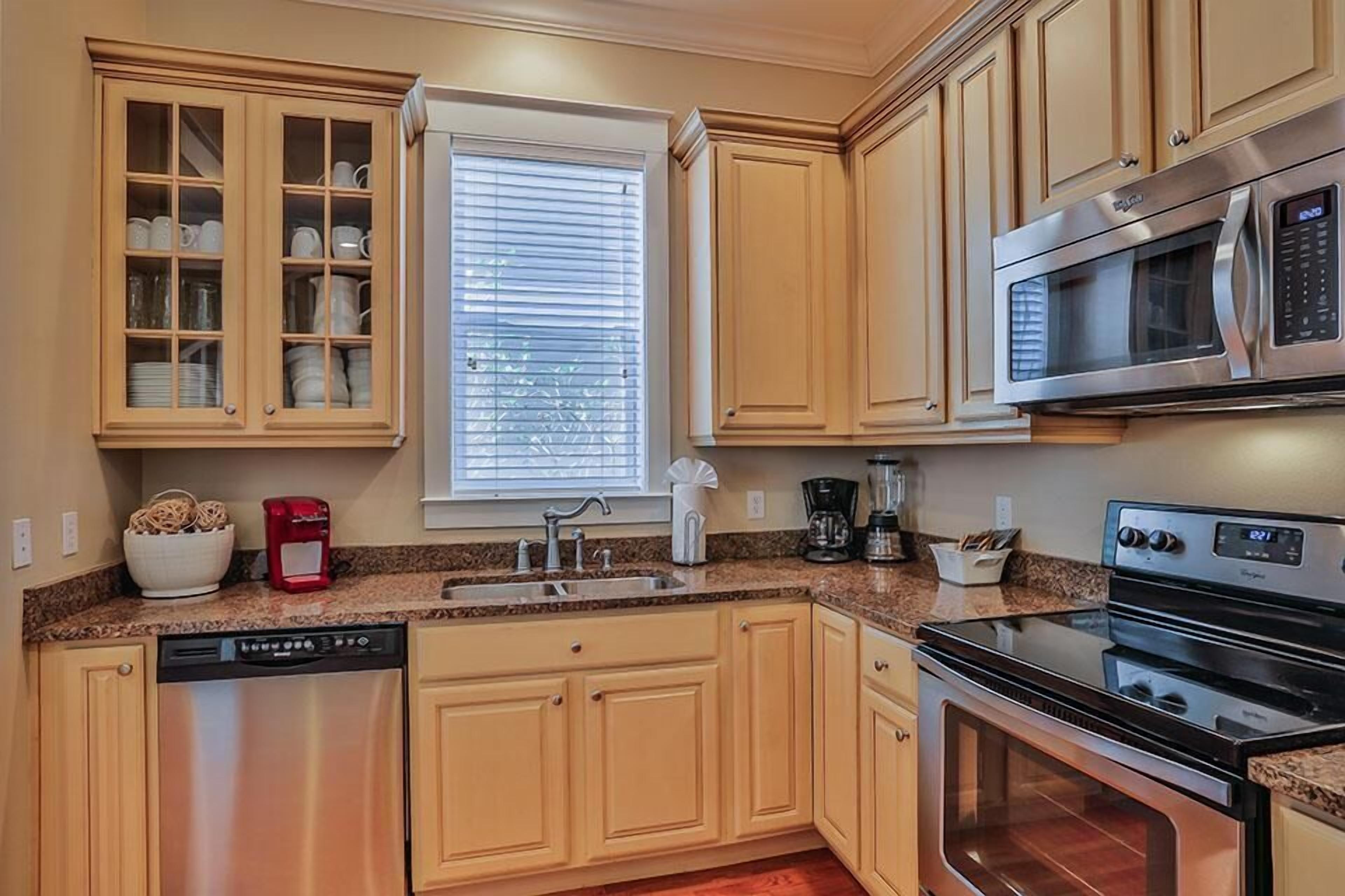A kitchen with wooden cabinets, a dishwasher, a microwave, a stove, and a window with blinds.