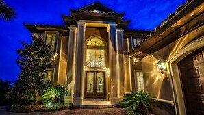 Une grande maison à deux étages, dotée d’une entrée imposante, d’un balcon et d’une allée bien éclairée.