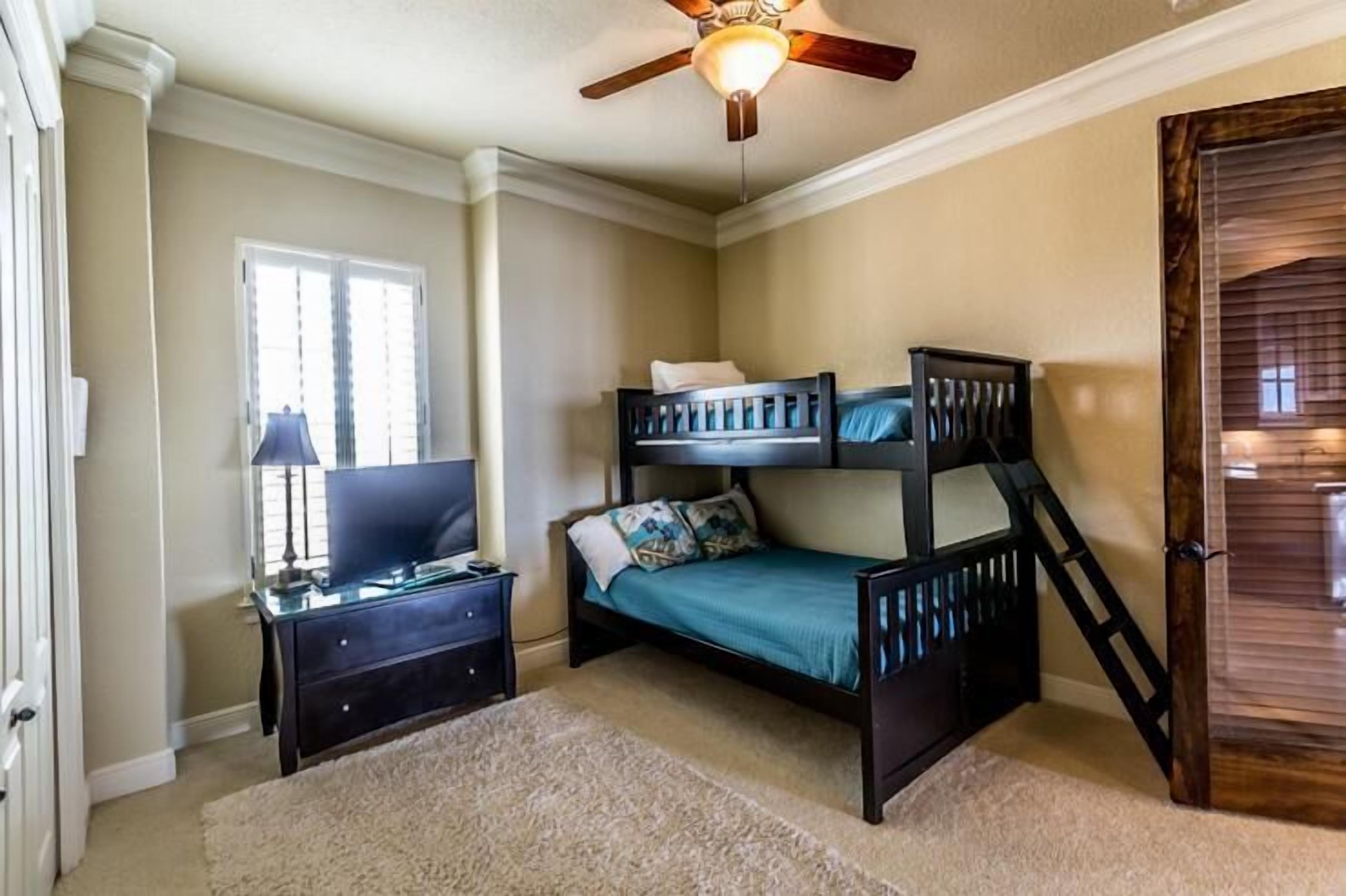 A bedroom with a bunk bed, a desk with a lamp, and a ceiling fan.