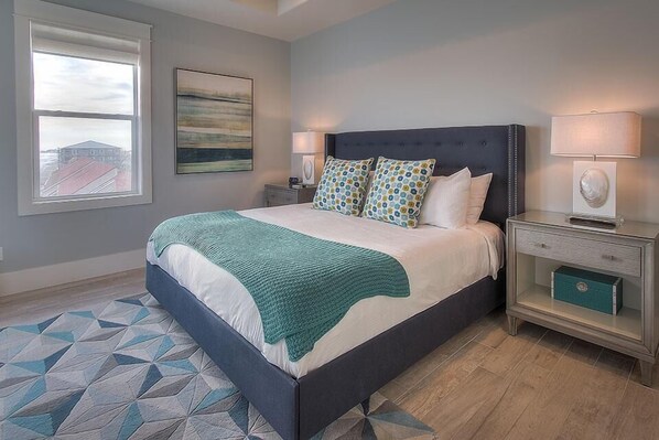 A bedroom with a bed, nightstands, a lamp, a painting, and a geometric rug.