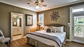 A bedroom with a bed, a nightstand, a chair, a ceiling fan, and a door with a view.