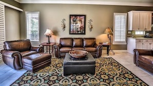 A spacious living room with a brown leather sofa, a matching armchair, and a patterned rug.