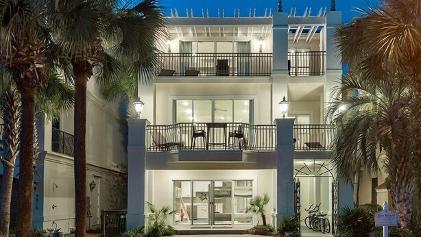 A two-story hotel with a balcony on the upper floor, palm trees in the foreground, and a bicycle parked outside.