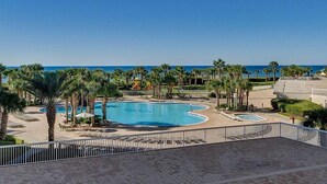 Une piscine d’un complexe hôtelier, bordée de palmiers, avec un ciel bleu azur et une vue sur l’océan.