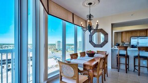 A dining area with a large table, chairs, and a view of the city through large windows. - ST LUCIA 1006 3 Bedroom Holiday Home by Five Star Properties (Destin)