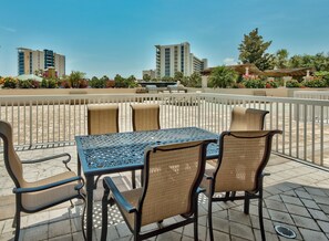 An outdoor patio with a table and chairs, surrounded by a white fence, overlooking a cityscape with tall buildings and greenery.