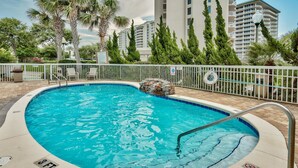 Ein Pool mit einer Tiefenmarkierung von 3 Fuß, umgeben von einem weißen Zaun, Palmen und hohen Gebäuden im Hintergrund.