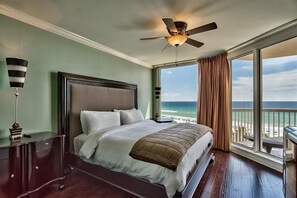 A hotel room with a large bed, a ceiling fan, a nightstand, and a view of the ocean.