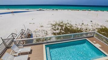 Uma piscina com um deck, espreguiçadeiras e vista para uma praia e oceano.