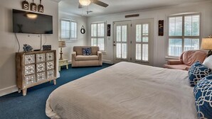 A bedroom with a large bed, a ceiling fan, a TV, and a cabinet.