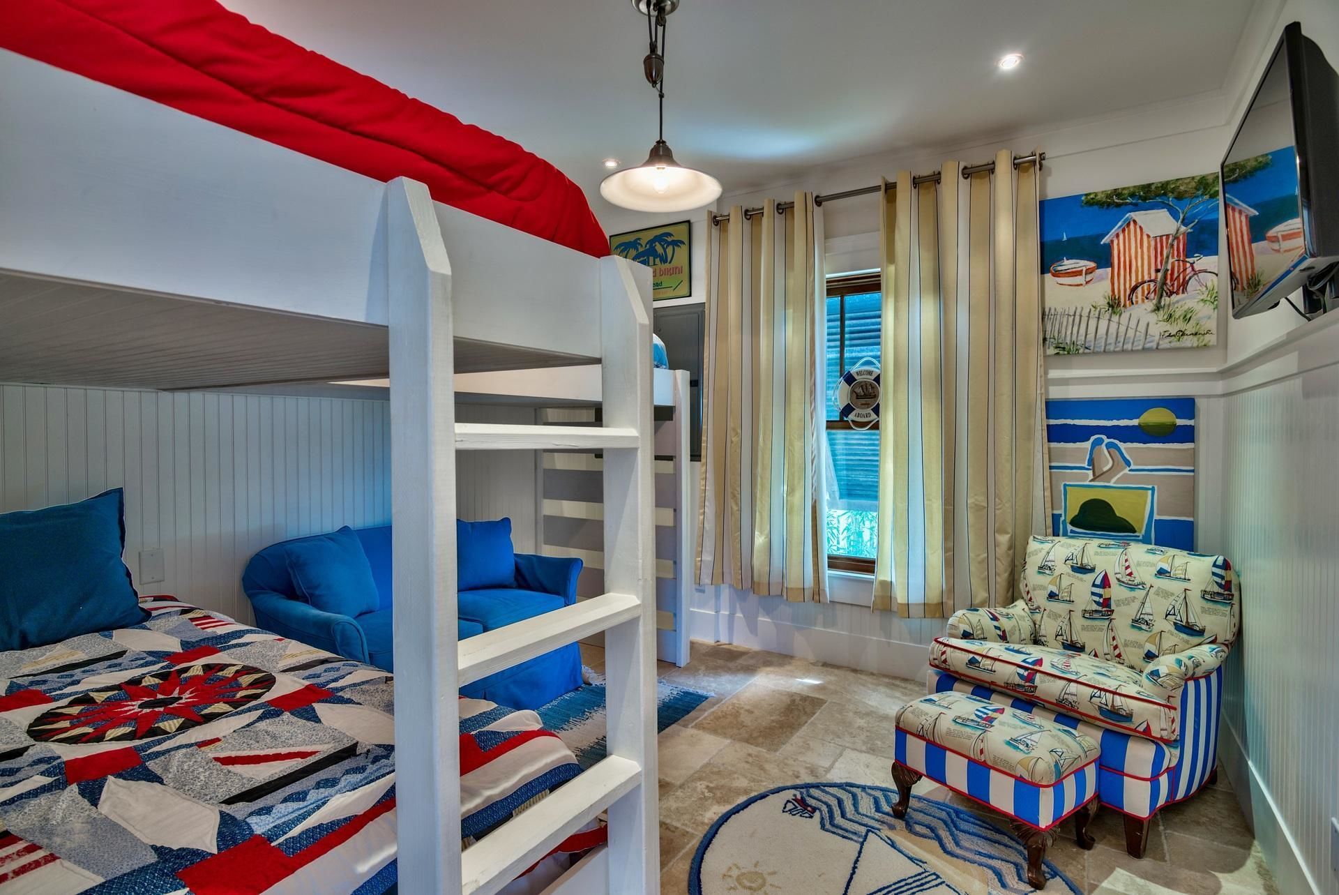 A room with bunk beds, a chair with nautical-themed upholstery, and a wall mural depicting a beach scene.