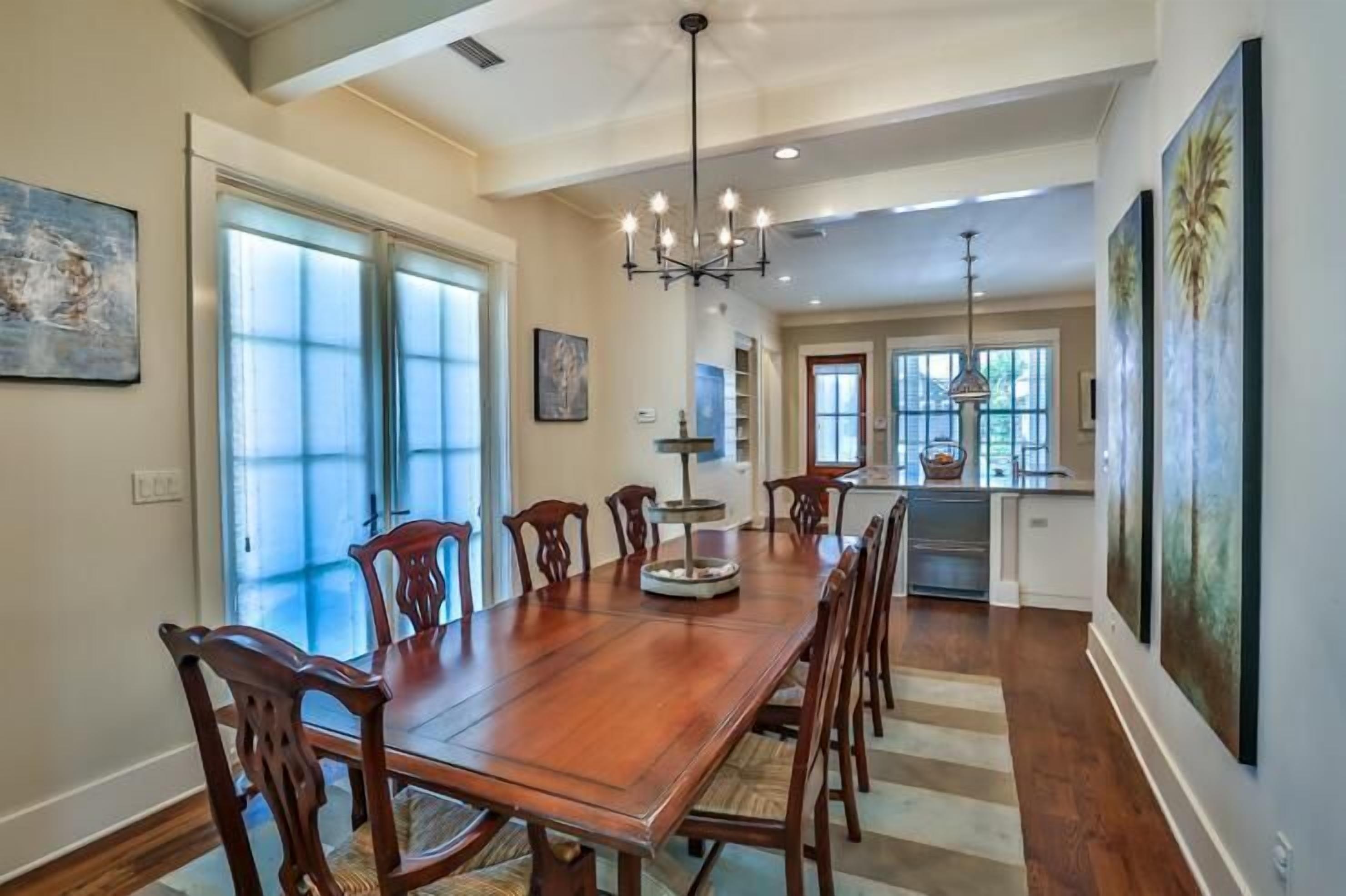 A spacious dining area with a long wooden table, multiple chairs, and a chandelier.