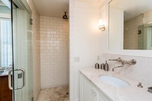 Ein modernes Badezimmer mit Duschkabine aus Glas, einer weiß gefliesten Duschfläche, einem großen Spiegel und einer Marmorplatte mit Waschbecken.