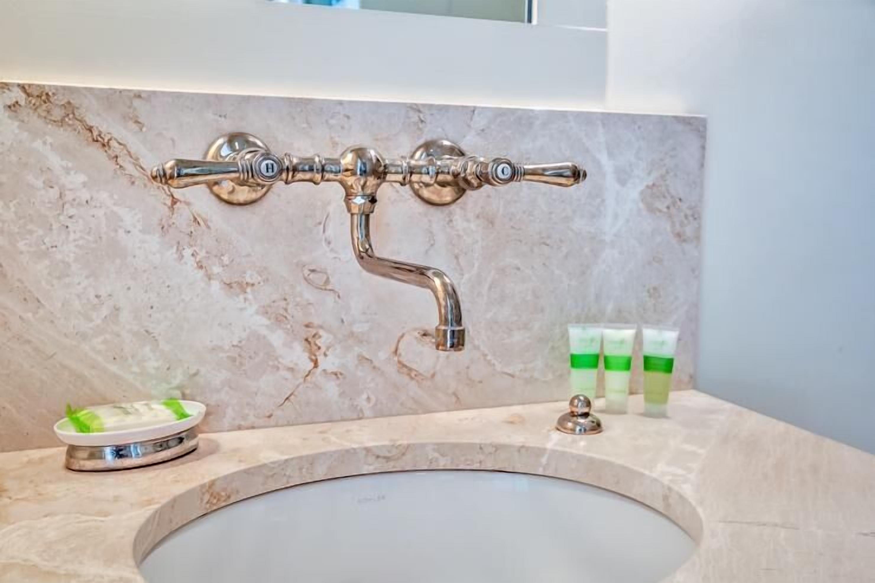 A bathroom with a marble sink, a wall-mounted faucet, and a soap dispenser.